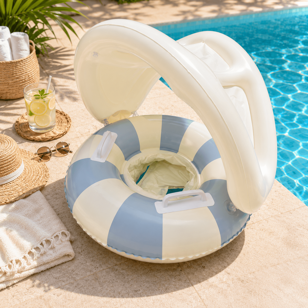An inflatable pool float with a white canopy and blue-and-cream striped ring, styled by a swimming pool with beach accessories like a straw hat, sunglasses, a drink, and a towel.